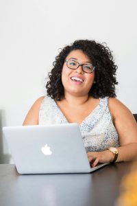Client Stories Happy businesswoman with curly hair using a laptop at her desk, smiling confidently.